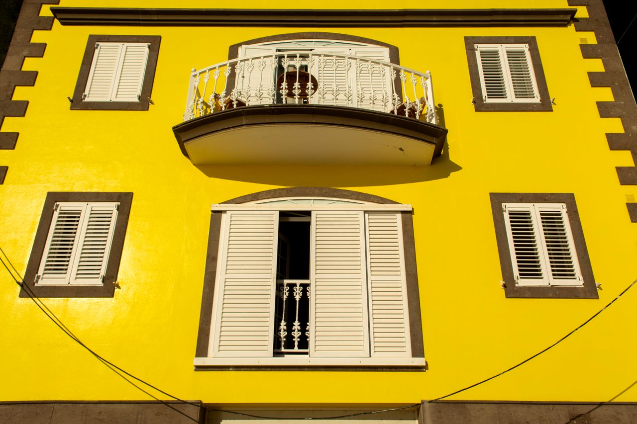 A bright yellow building facade with a retro balcony and shutters.