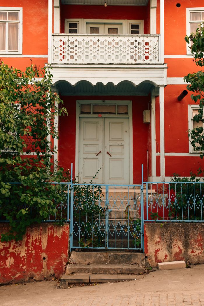 Vibrant red townhouse facade with intricate white balcony and blue gate, showcasing urban architecture.