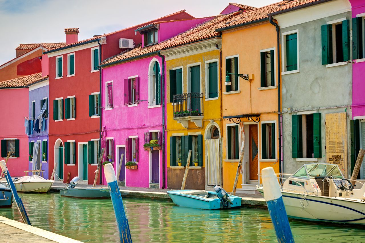Vibrant canal-side houses in Burano, Italy, featuring colorful facades and docked boats.