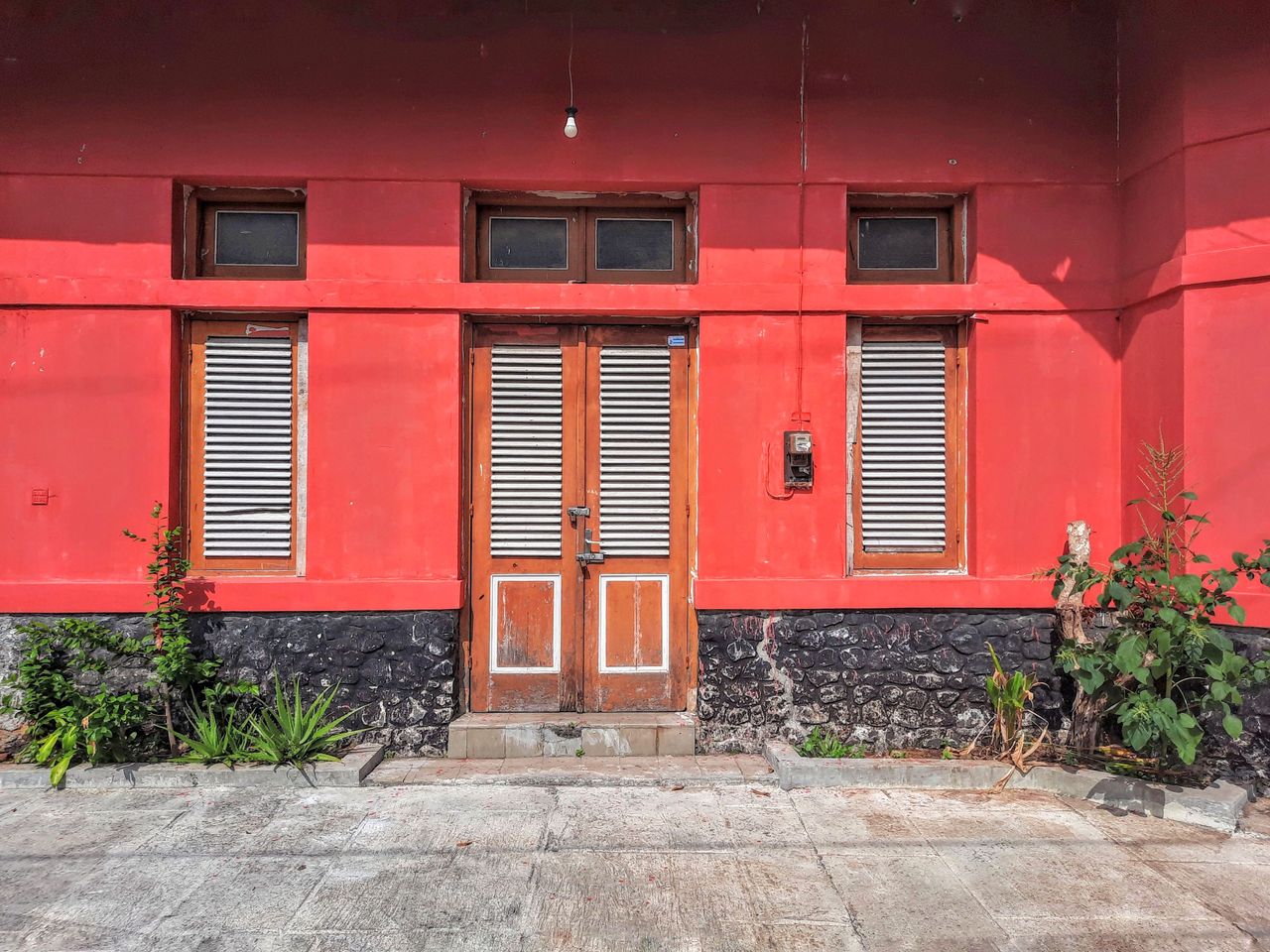 A vibrant red building facade features wooden shutters and a dual-door entrance.